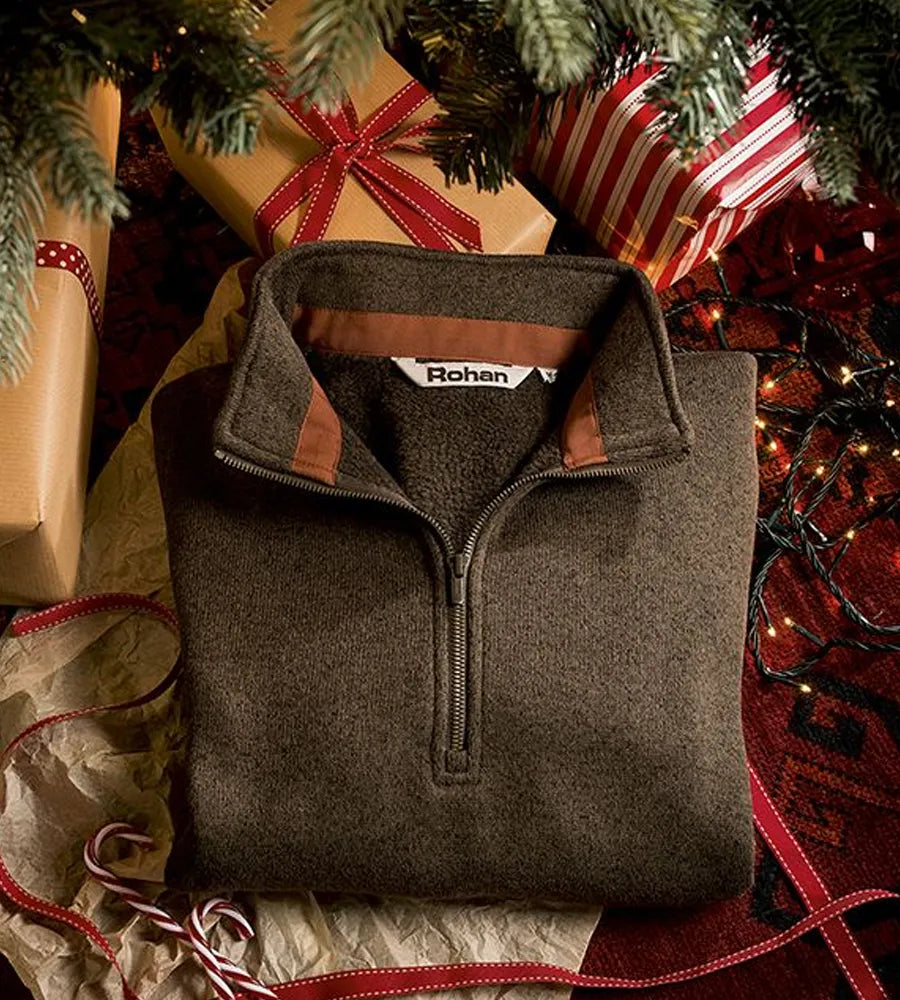 Brown pullover with a brand label on a Christmas-themed background with presents and lights.